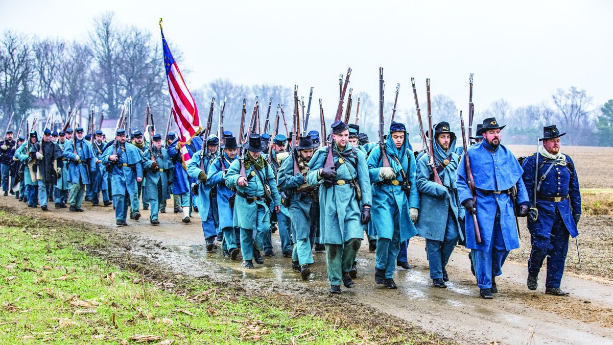 Union reenactors march in freezing temperatures while snow flurries fall.